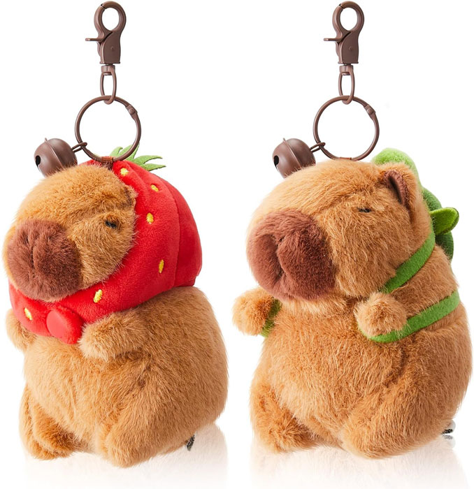 Two capybara plush keychains with clip attachments, one wearing a strawberry hood and the other a turtle backpack.